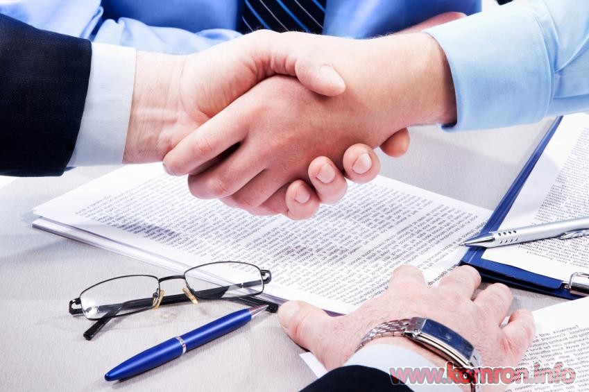 Close-up of business handshake over workplace with documents, pens, glasses